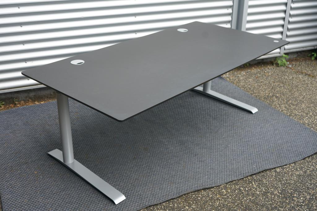 Cube Design hæve-sænkebord 180x90 cm med sort linoleum bordplade og gråt stel, set fra skrå vinkel.